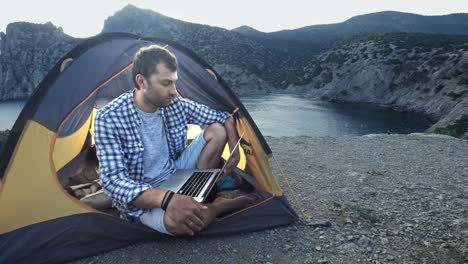 freelancer man working using laptop sitting in a camping tent on the beach. freelancer working on new startup project using laptop computer and wireless connection. freelance summer travel.