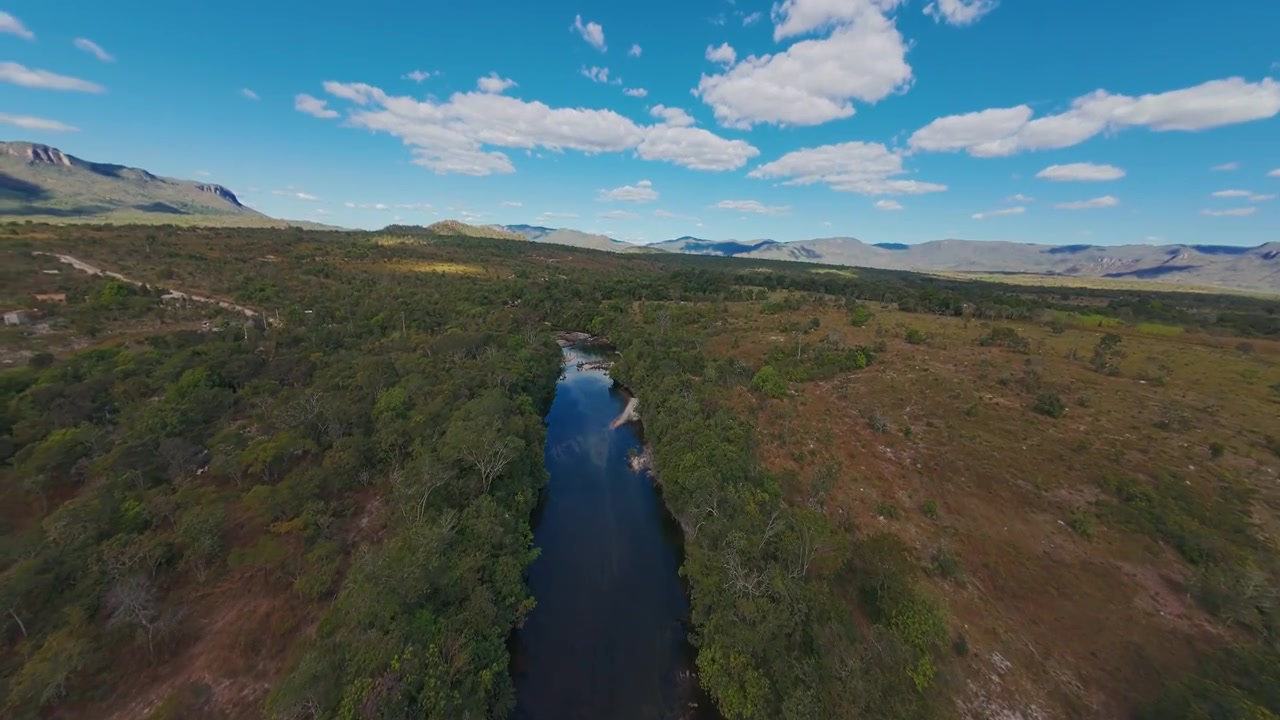 O Rio Alma flui por uma densa mata de Cerrado sob um vasto terreno montanhoso perto de Cavalcante, Goiás, Brasil, com uma perspectiva de baixo nível do rio em um sobrevoo rápido de drone FPV