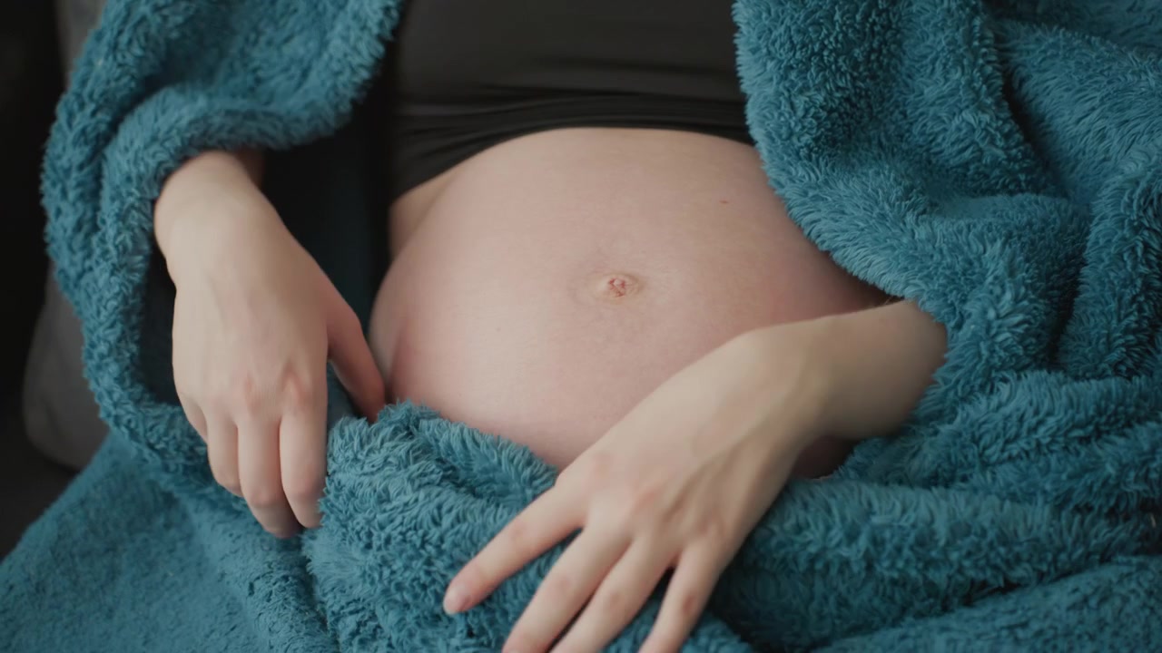 Donna incinta che tocca delicatamente la pancia sotto una coperta blu