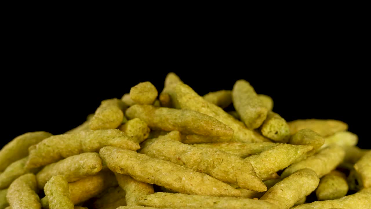 Crispy green pea puff snacks in a pile, slow macro zoom, black background, studio lighting