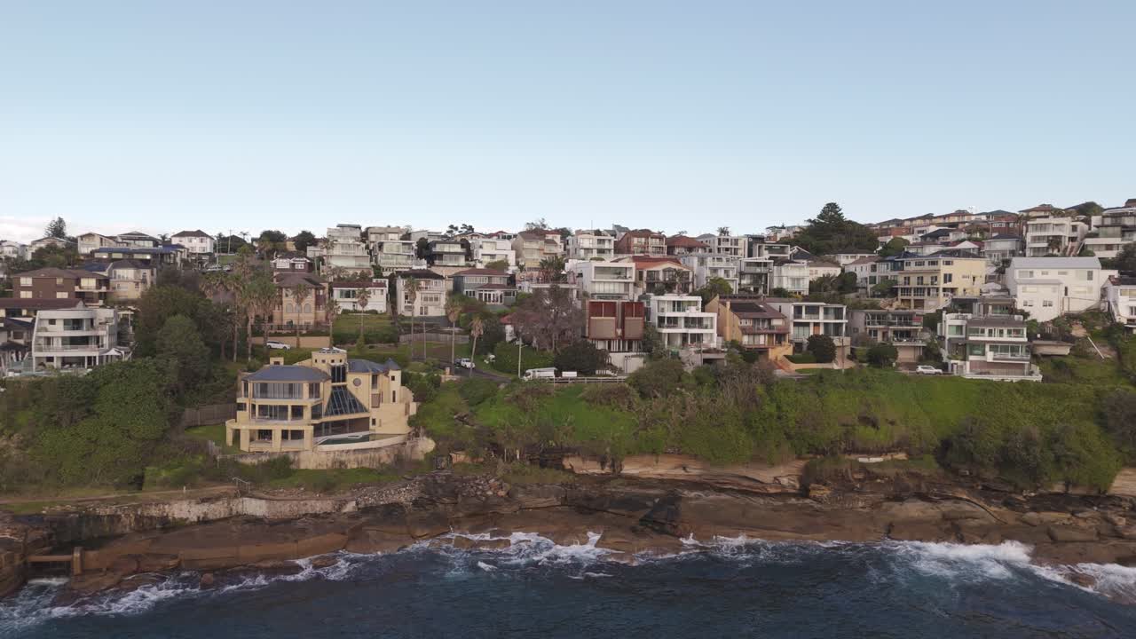 Aerial Drone Slide Right Over Sydney Oceanfront Mansion – Cliffside Waves, Blue Water, Luxury Rooflines, Coastal Neighborhood, Morning Sky in NSW