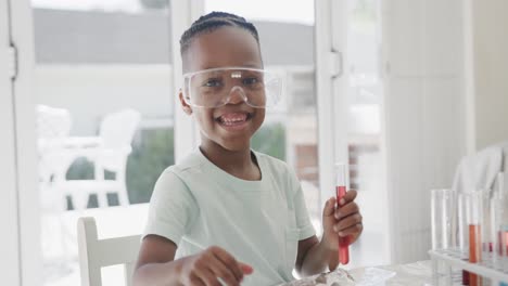 Portrait-of-african-american-boy-sitting-at-table-holding-test-tubes-with-liquid,-in-slow-motion