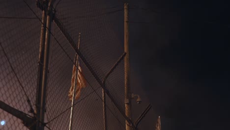 american flag blowing behind a fence surrounded by smoke at night time