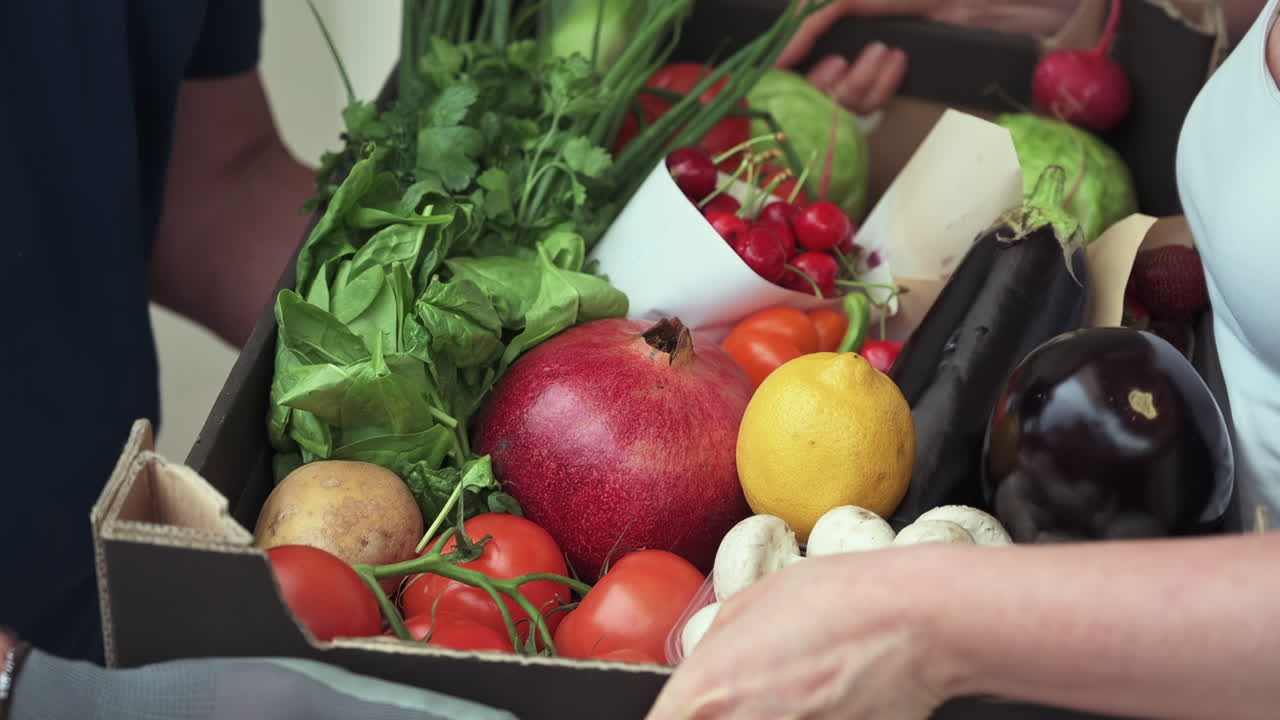 Woman receiving a box of fresh fruits and vegetables from a masked delivery man