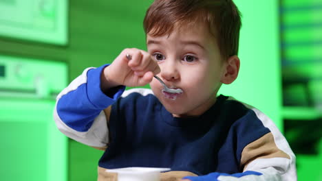 beautiful caucasian toddler boy eating yogurt. baby consuming dairy with appetite. close up.