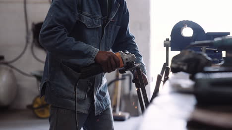 young black male with denim jacket using angle grinder power tool in workshop with sparks