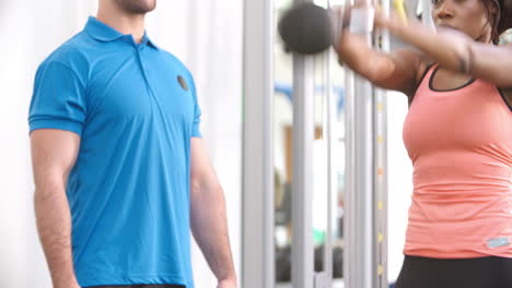 woman exercising with a kettlebell in a gym with a trainer