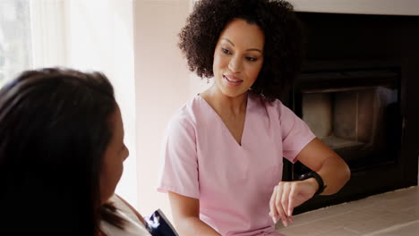 nurse in pink scrubs checking smartwatch while talking to patient