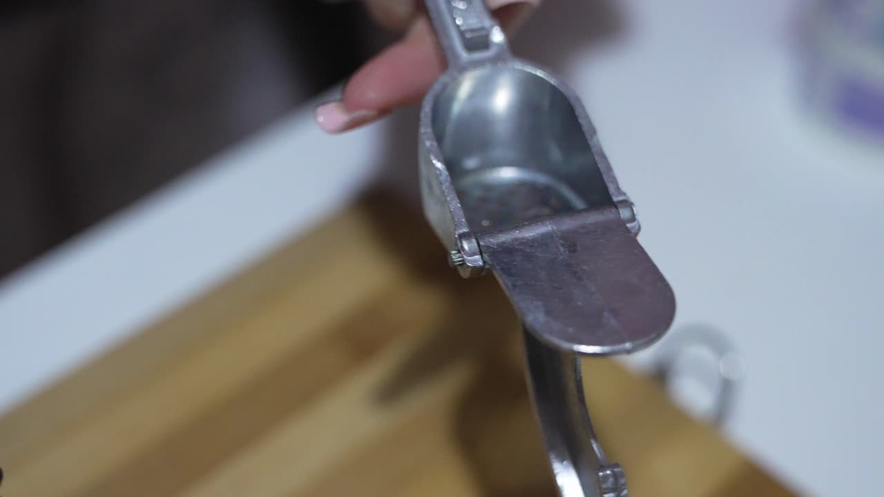 Close up of hands using a metal garlic press to crush fresh garlic cloves for cooking.