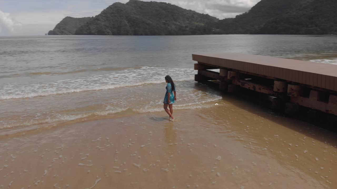 섹시한 여자가 산을 배경으로 해변의 해안선에서 몸을 구부린다