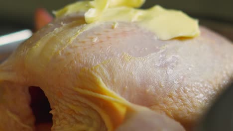 close up details of raw whole organic chicken with soft butter on top ready to go in oven to roast. high protein lean meat.