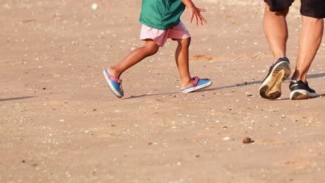child and adult running together on sandy beach
