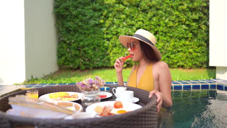 Asian-woman-having-lunch-inside-swimming-pool,-pick-up-watermelon-from-floating-tray,-slow-motion