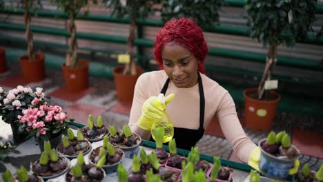 Young-indian-woman-watering-flower-in-a-greenhouse---eco-hobby-concept