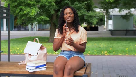 Concepto-De-Tecnología,-Educación-Y-Personas-Feliz-Y-Sonriente-Estudiante-Afroamericana-Con-Libros-De-Texto-Llamando-A-Un-Teléfono-Inteligente-En-La-Ciudad