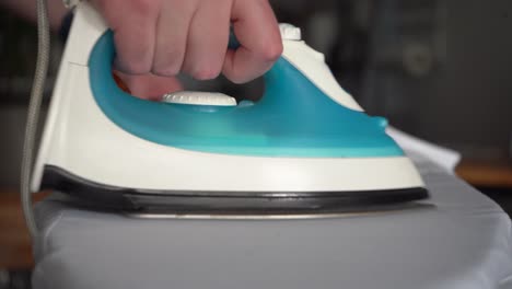 narrow focus young caucasian man irons white shirt on ironing board