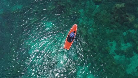 Vista-Superior-De-Un-Hombre-Sentado-En-Una-Tabla-De-Remo-Y-Remando-Sobre-Una-Laguna-Azul-Clara-Con-Un-Hermoso-Arrecife-De-Coral-Bajo-El-Agua