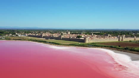 the historical town of aigues-mortes in the camargue, france during a sunny summer day which is located next to a pink salt lake