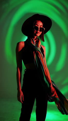 stylish woman in hat and colorful scarf posing under artistic green and red lighting