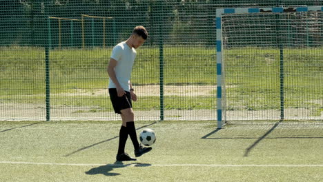 a young soccer man training freestyle tricks with the ball on a street football pitch on a sunny day