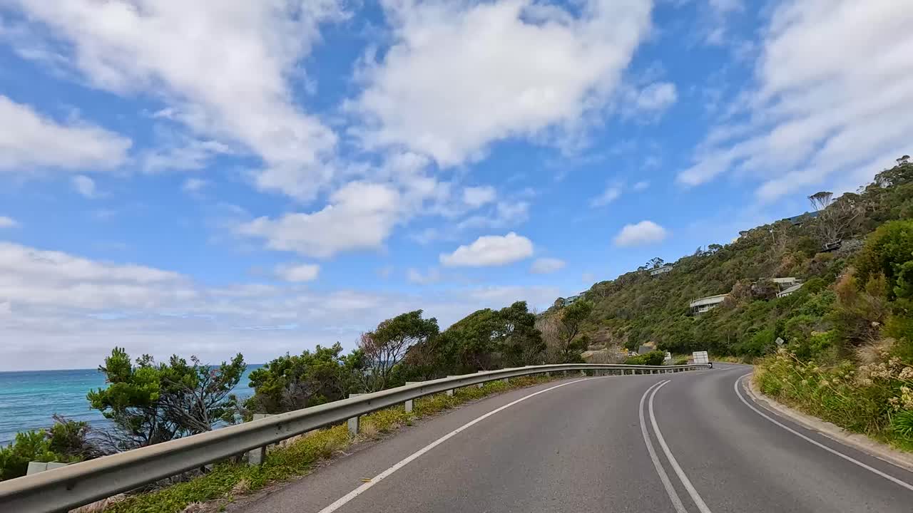 A serene drive along the Great Ocean Road, showcasing coastal views, lush greenery, and a clear blue sky