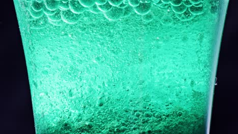 macro shot of a glass with many blue bubbles floating and dripping in water