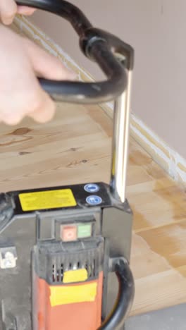 hand switching on electric floor sanding machine on wooden flooring restoration, vertical