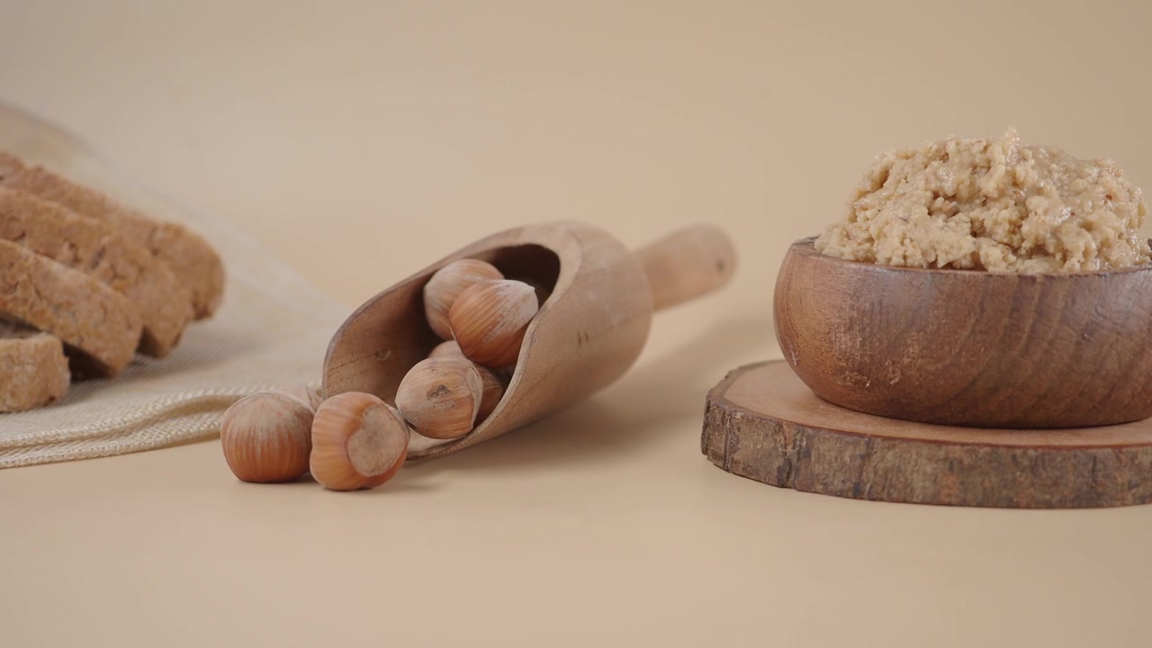 Burro di nocciole in ciotola di legno con nocciole intere e pane