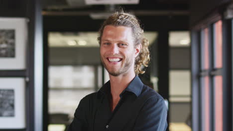 millennial white male business creative smiling to camera by the window in an office, close up