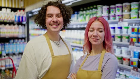 Portrait-of-supermarket-workers.-A-brunette-guy-and-a-girl-with-pink-hair-posing-near-the-department-with-dairy-products-in-the-supermarket