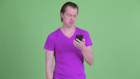 fotografía de estudio de un joven triste usando un teléfono móvil contra un fondo verde