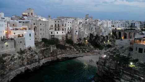 Eine-Drohne,-Die-Die-Klippe-Von-Polignano-Im-Sonnenuntergang-Vom-Einzigartigen-Stadtstrand-Aus-Enthüllt