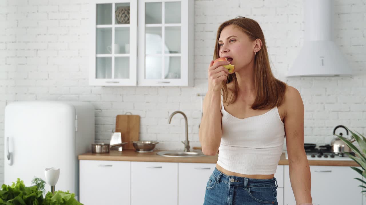 Young sports girl in white is biting a fresh red apple. Healthy food. Healthy vegan with fruits