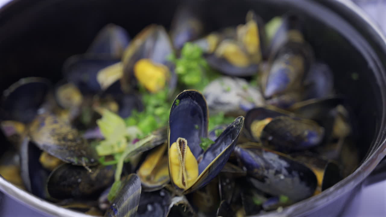 Close up of multiple steamy mussels in a pot with green onions on top