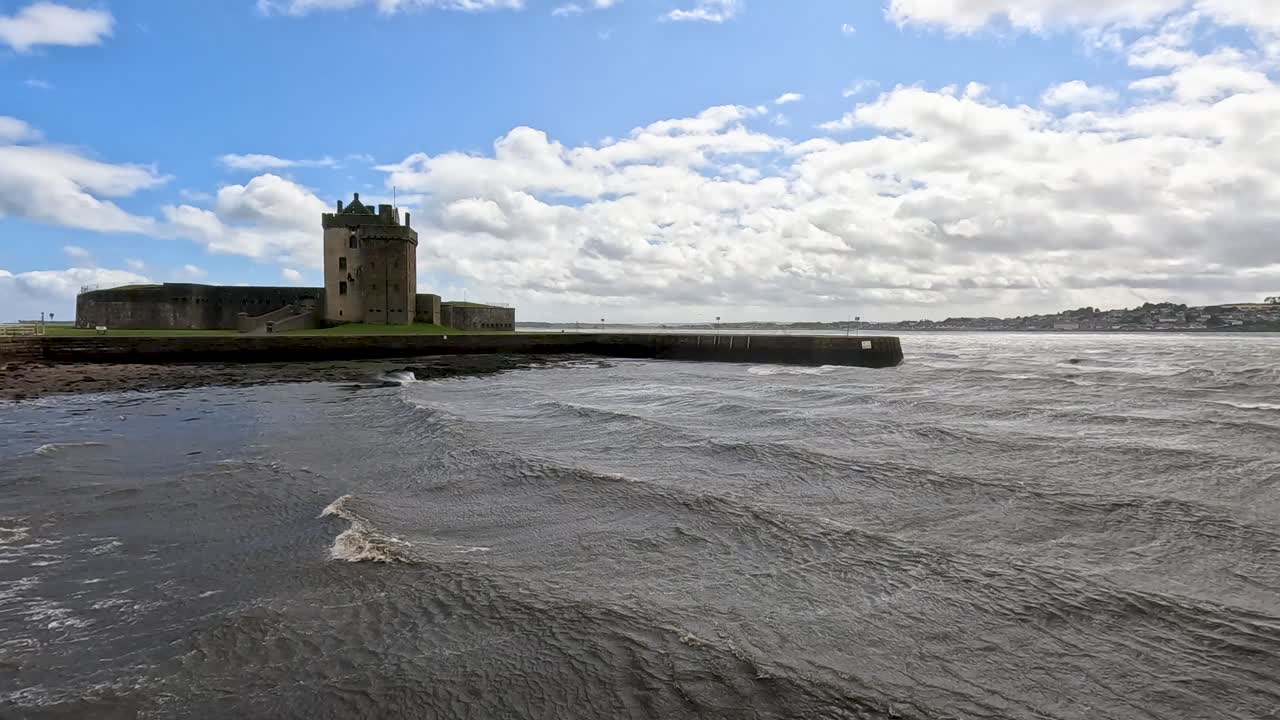 Wide view of historic coastal castle with gentle waves, partly cloudy sky, and natural daylight