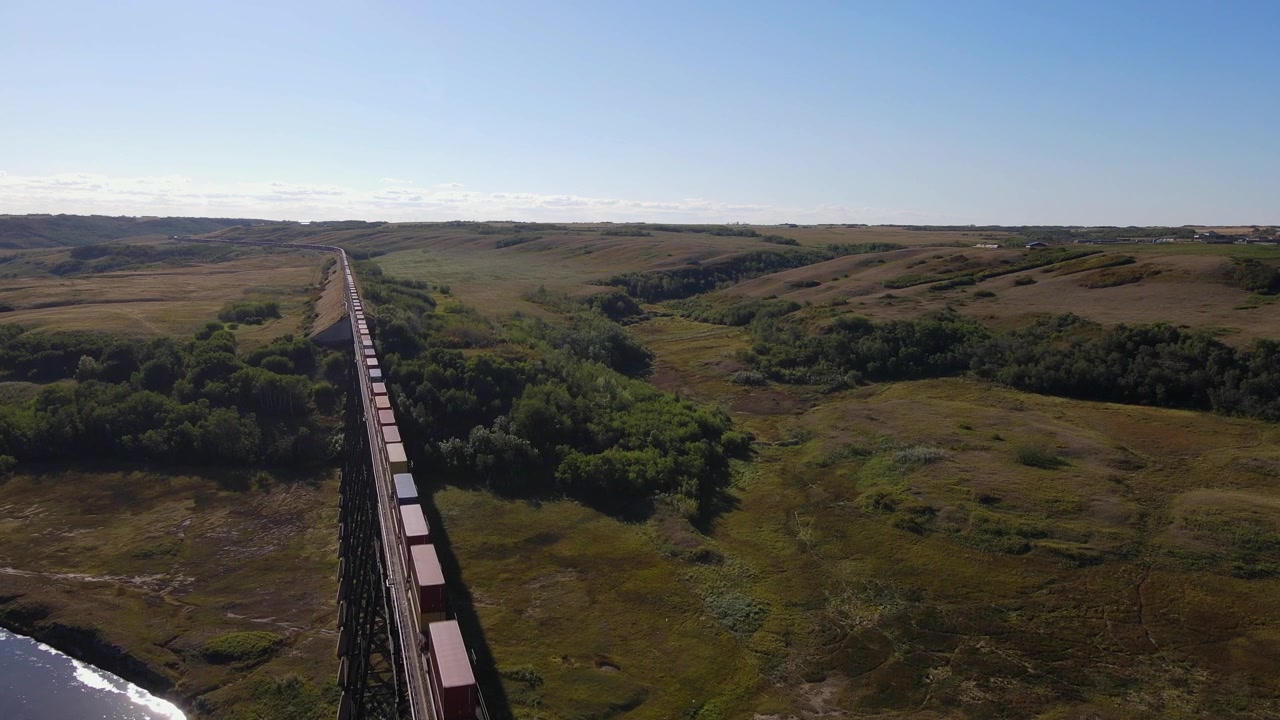 Záběry z dronu mostu Battle River Trestle Bridge ve Wainwrightu, Alberta. Blížící se vlak, slunečný den, modrá obloha.