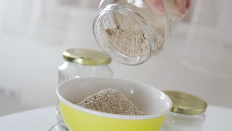 pouring out almond wheat into a bow from a glass jar in the kitchen