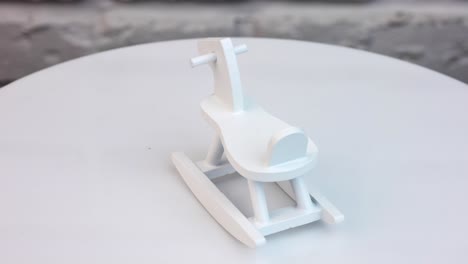 wooden rocking horse rotating at the table. small toy decoration for the doll's house interior. white wall background.