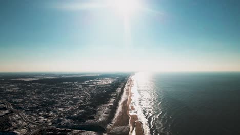 The-sea-meeting-snowy-dunes-under-a-bright-sun-in-the-netherlands,-aerial-view