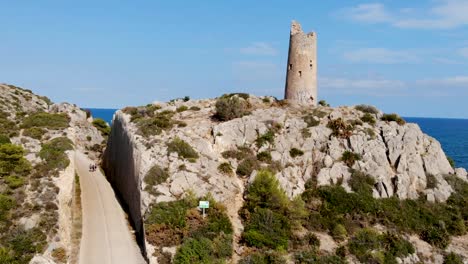 drone vuela sobre una torre de vigilancia costera, una torre centenaria en el acantilado marino y el cielo azul con rocas en una pasarela costera