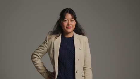 smiling businesswoman in beige blazer and blue sweater posing in studio