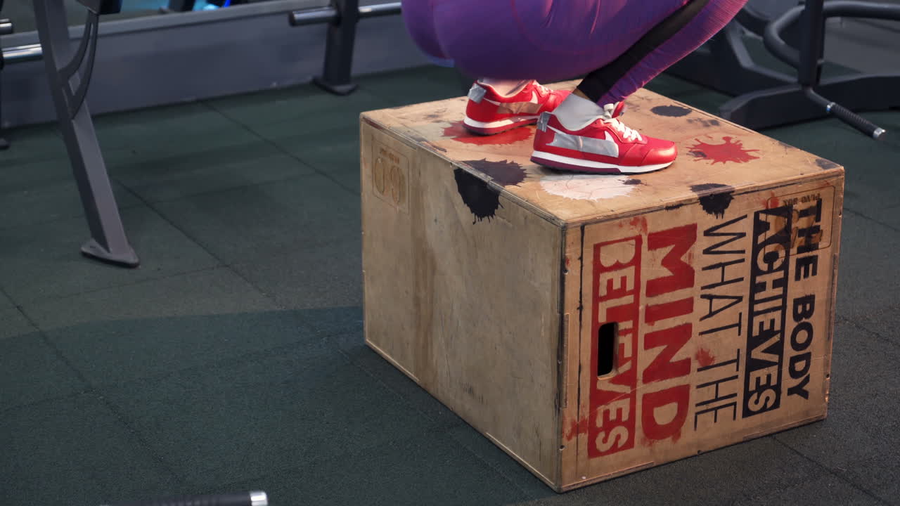 Ragazza che salta in palestra. Atleta donna che esegue salti sulla panca in palestra con focus sulle gambe