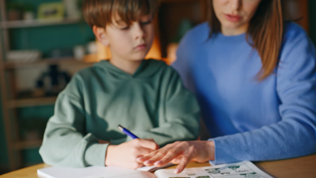 Primo piano delle mani del tutor che sfogliano le pagine di un libro di testo delle scuole elementari, aiutando l'alunno.