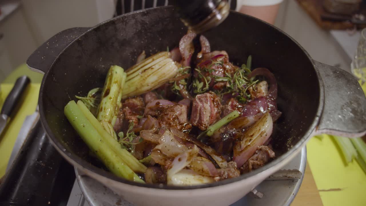 혼합 쇠고기 정강이, 양파 조각, 셀러리 및 향신료가 있는 깊은 요리 냄비에 발사믹 식초를 추가