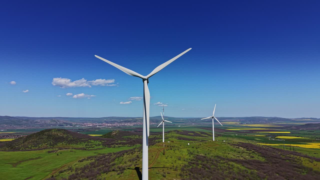 Pale eoliche su una collina verde dominano una piccola città sotto un cielo blu