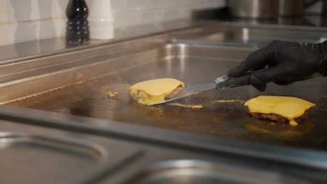 Hands-of-chef-with-spatula-taking-delicious-cheeseburger-patty-from-hot-stove,-static-shot