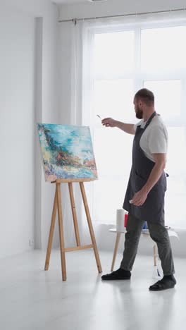 a talented artist using a brush creates a modern masterpiece of oil painting - a talented artist, using a brush, creates a modern masterpiece of oil painting. creative studio with canvas of bright colors. close-up. high quality full footage