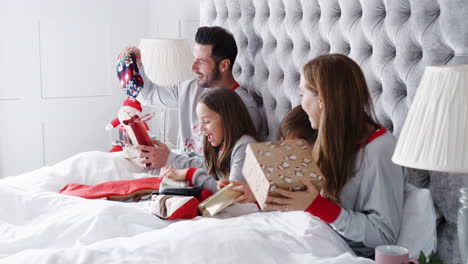 excited family in bed at home together opening gifts on christmas day
