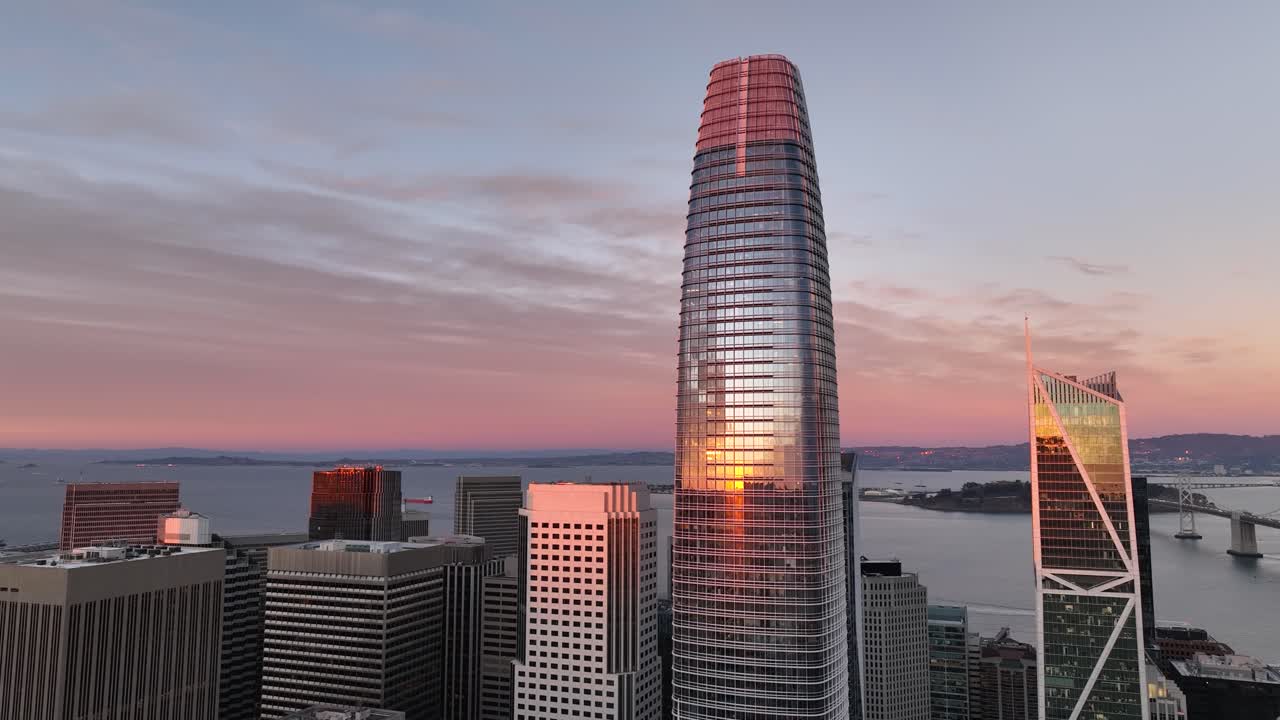 panorámica aérea de la torre salesforce con el reflejo de la puesta de sol y el puente de la bahía de oakland