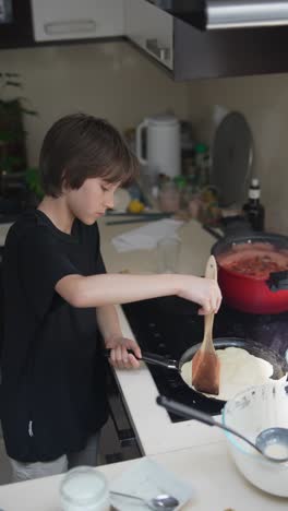 young boy making pancakes in kitchen